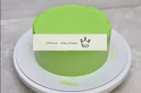 从冰箱里取出蛋糕，从戒指和胶卷中取出。在蛋糕的侧面和顶部涂上绿色奶油。用马刺将蛋糕夷为平地。让上边缘...